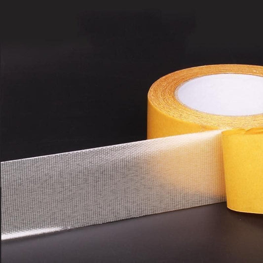 Roll of heavy duty carpet adhesive tape with mesh reinforcement and yellow release liner for securing area rugs