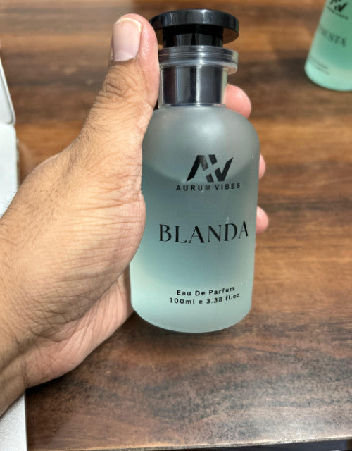 Hand holding Blanda male fragrance 100ml Eau De Parfum bottle by Aurum Vibes on wooden surface