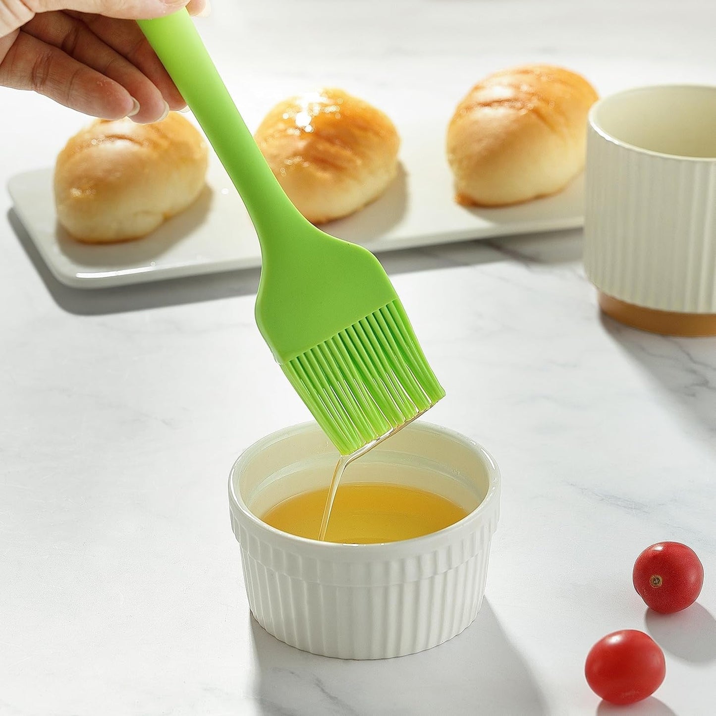 Green oil brush dipping into oil with fresh bread rolls in background best baking basting brush