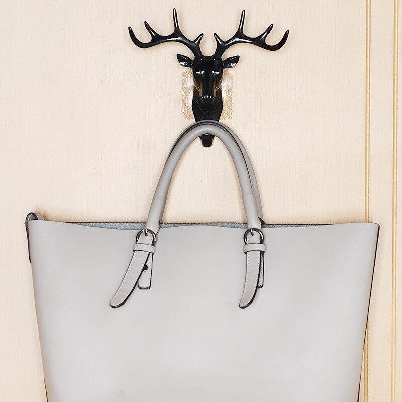 Black deer head self adhesive coat hook holding a gray handbag on a beige wall