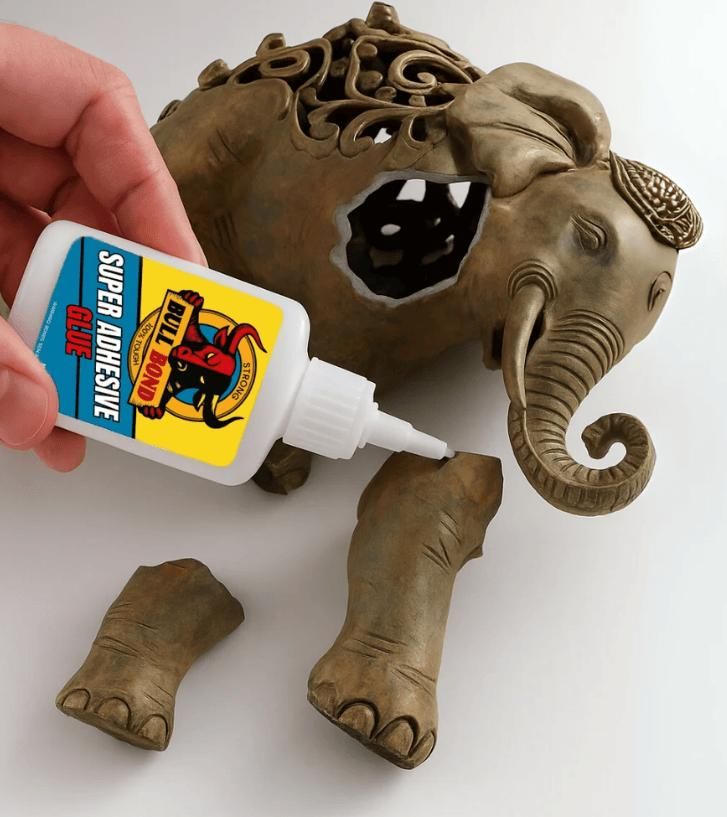 Hand applying strong bonding glue for home use to reattach broken ceramic elephant figurine legs