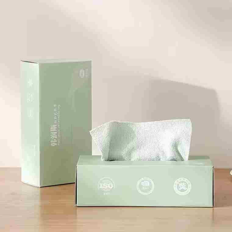 Pastel green extractable household cleaning wipes box on wooden table with a white wipe pulled out and standing box in background