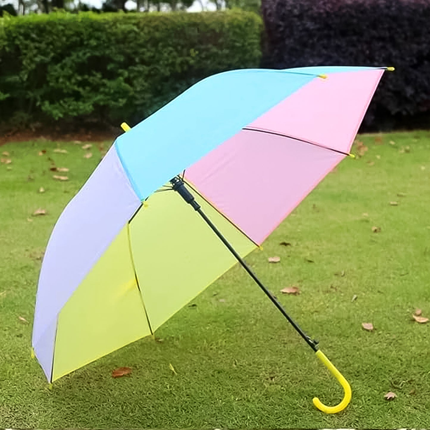 colorful rainbow umbrella with pastel panels and yellow curved handle on grass