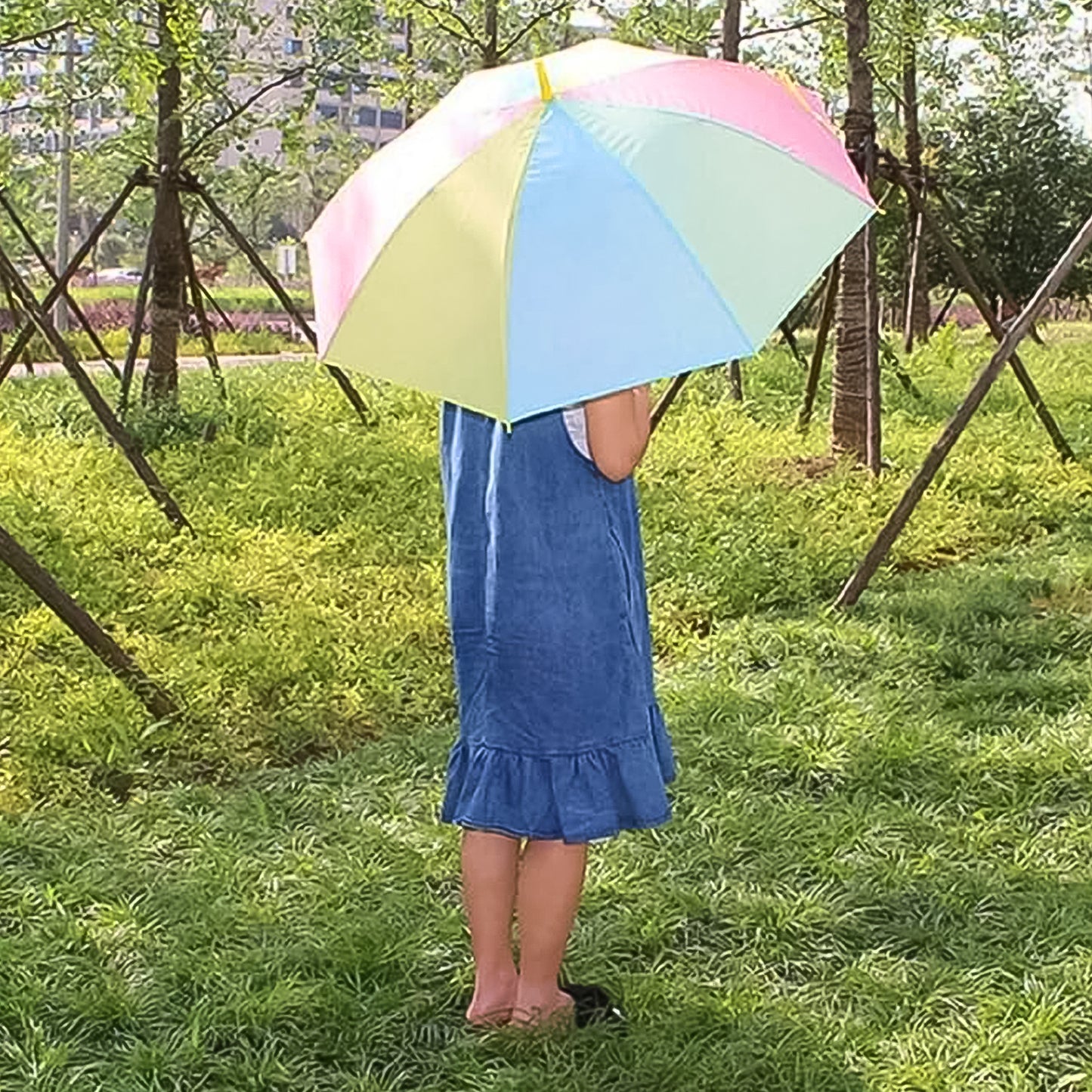 Person holding colorful rainbow umbrella outdoors in green park setting