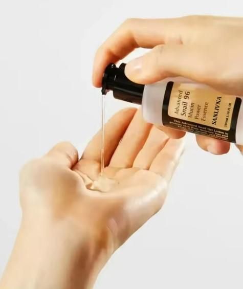 Applying snail mucin power essence from a bottle into a hand for skincare routine