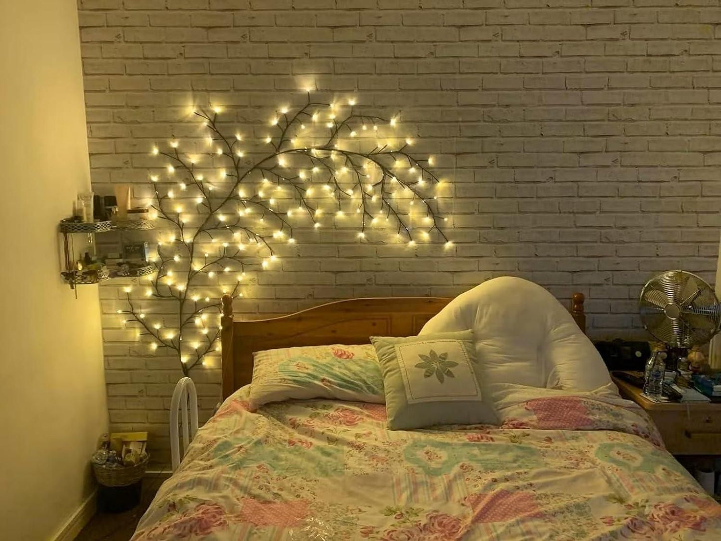 Decorative branch fairy lights twinkling above a cozy bed against a brick wall