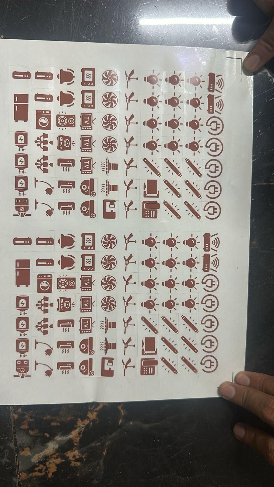 Pack of decorative light switch stickers featuring brown icons of lights, fans, plugs, and home appliances
