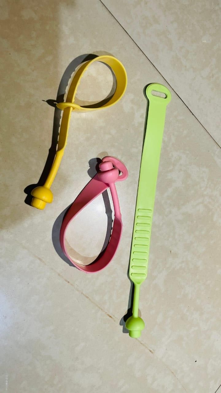 Set of three colorful hygienic toilet lid lifter tools in yellow, pink, and green on tiled floor