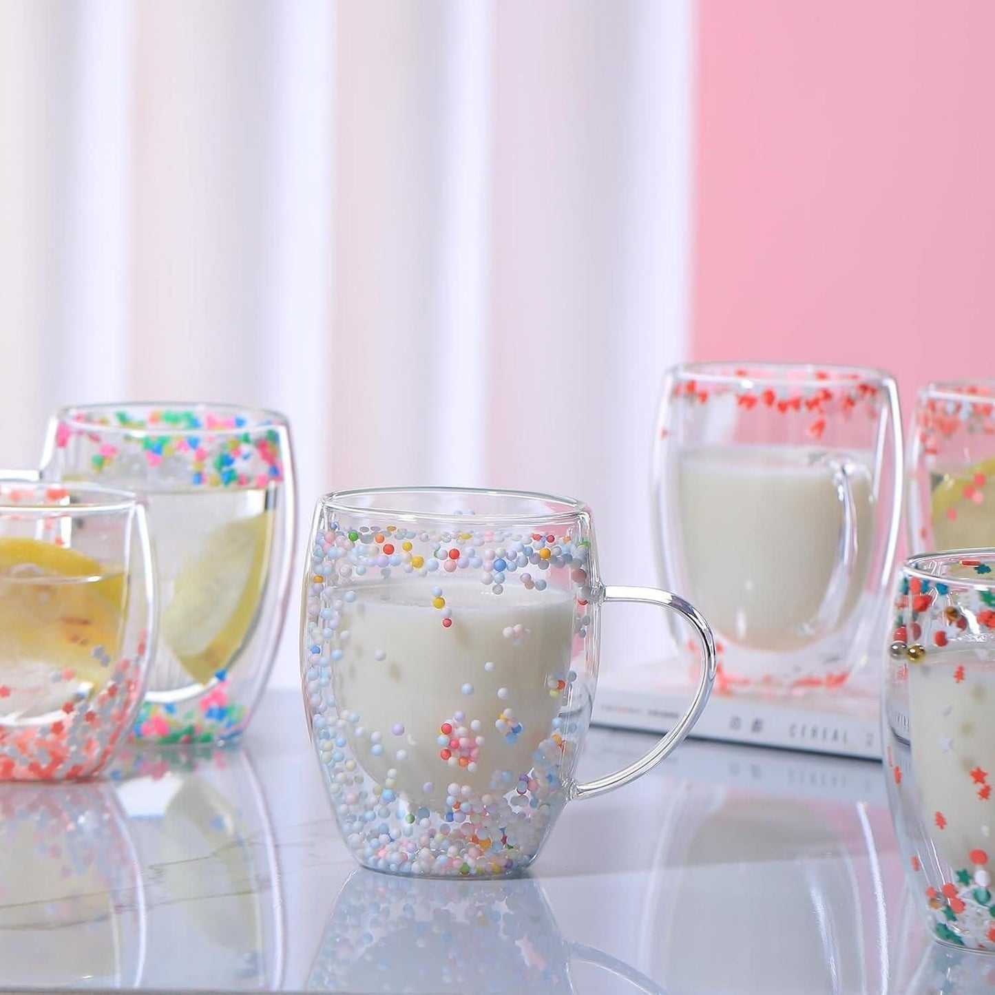 Colorful double walled glass coffee mug with sprinkles design filled with milk on a reflective surface