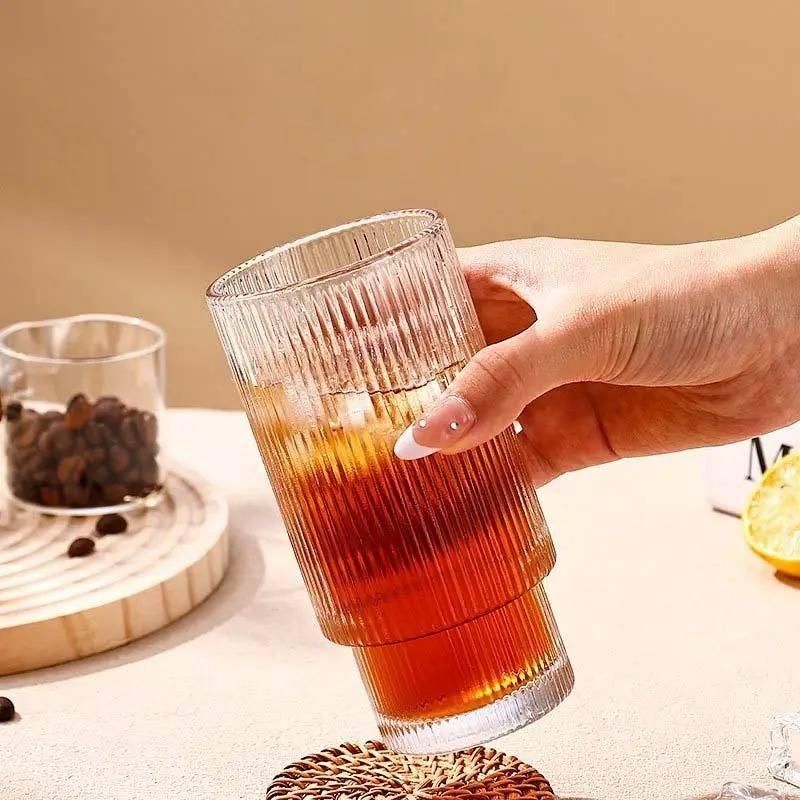 Product image of a ribbed clear glass filled with iced tea held by hand glass tumbler with wood cap nearby