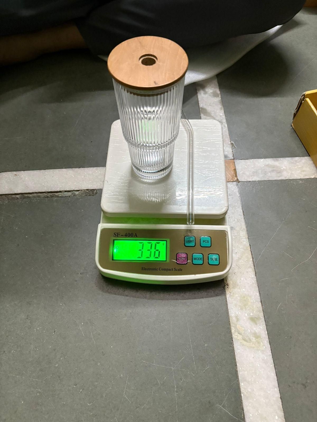 Ribbed clear drinking glass with wooden lid and straw on digital kitchen scale showing 336 grams
