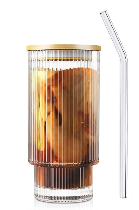 Ribbed glass tumbler with wood cap filled with iced coffee and cream swirl served with a clear glass straw