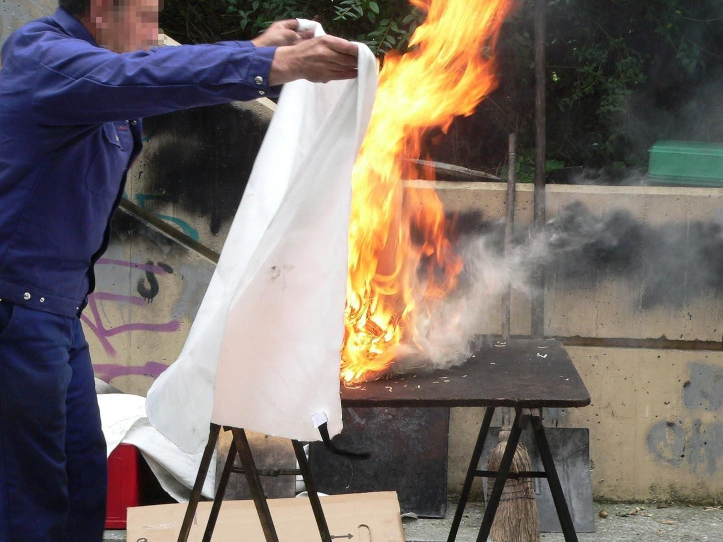 Person using a fire safety blanket for home to extinguish flames on a burning table outdoors
