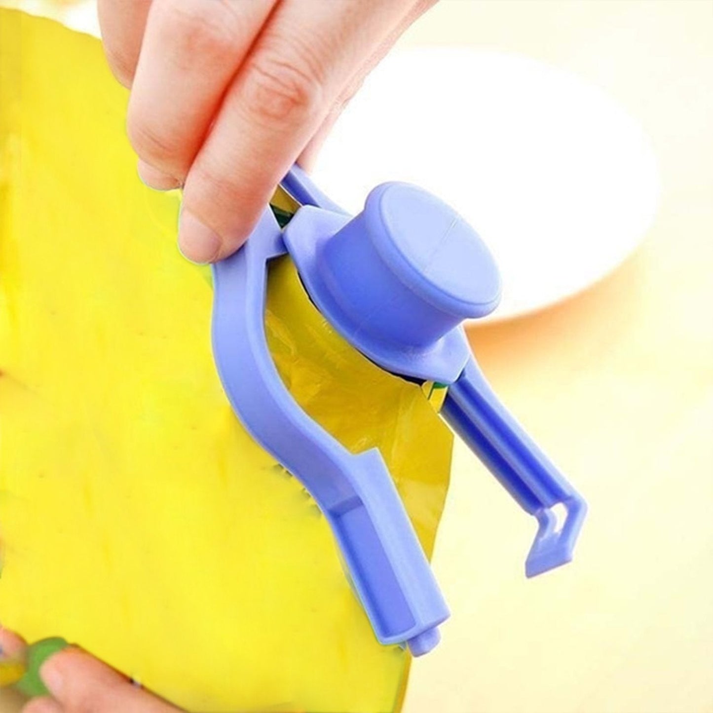 Hand using a purple food bag clip seal to securely close a yellow food storage bag