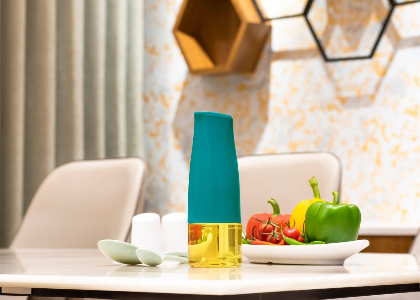Teal top and clear yellow oil dispenser bottle for kitchen on table with plate of peppers and tomatoes