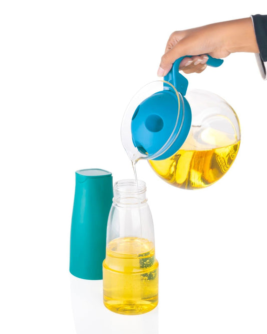Hand pouring olive oil from blue handled glass jug into clear refill container oil dispenser bottle for kitchen