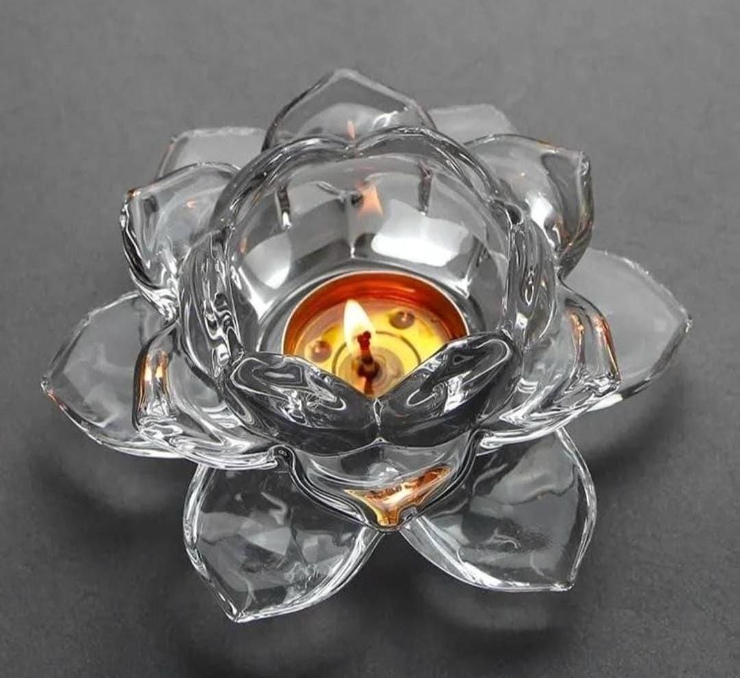 Clear glass lotus tea light holder with a lit candle inside on a dark background