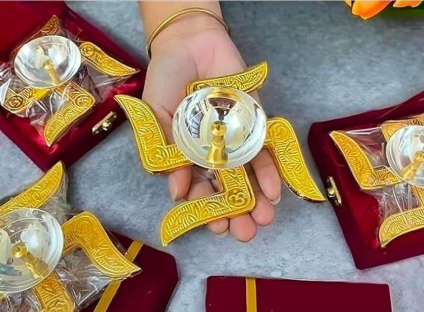 Hand holding handcrafted puja brass diya with intricate gold design displayed on red cloth
