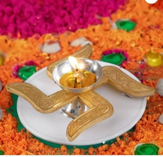 Handcrafted puja brass diya with intricate design lit and placed on a white plate surrounded by colorful flower petals