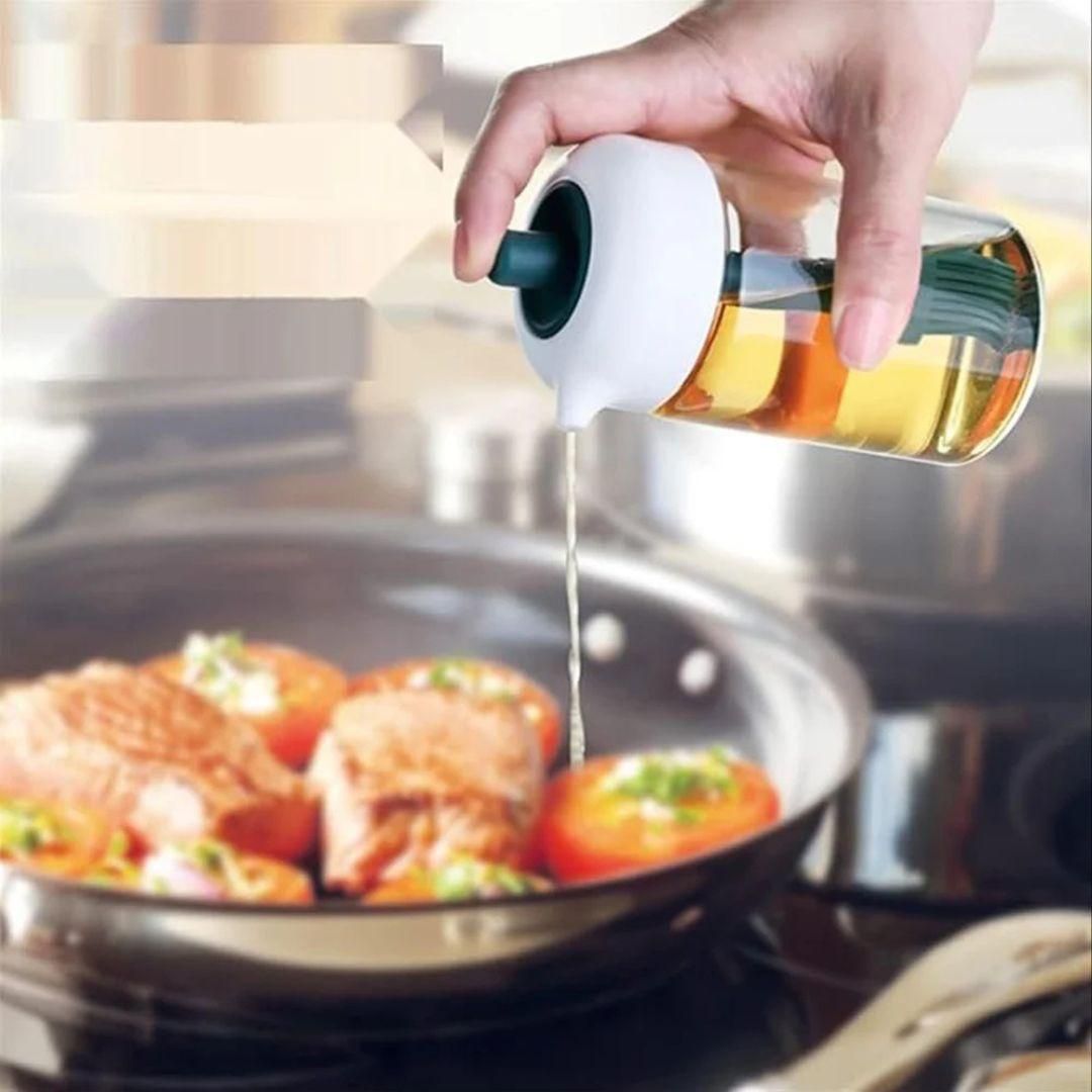 Hand pouring oil from glass bottle into pan with salmon and tomatoes oil dispenser for kitchen cooking