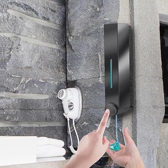 Black wall mounted soap dispenser dispensing blue liquid soap into hands on gray stone bathroom wall