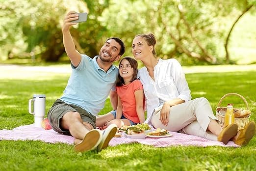 Family picnic with parents and child taking selfie on blanket and insulated sipper bottle with straw and handle nearby