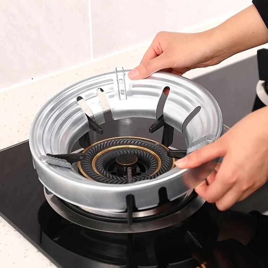 Hands installing a kitchen gas stove flame protector on a black stove burner