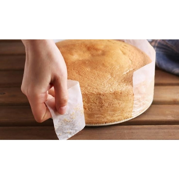 Your Brand microwave oven safe baking paper strips used to line and release a round sponge cake on wooden board