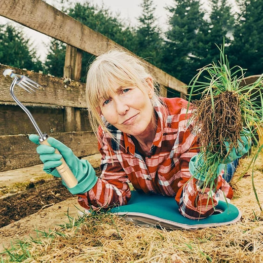 Woman using a manual weed remover for small farms while wearing gloves and a plaid shirt outdoors