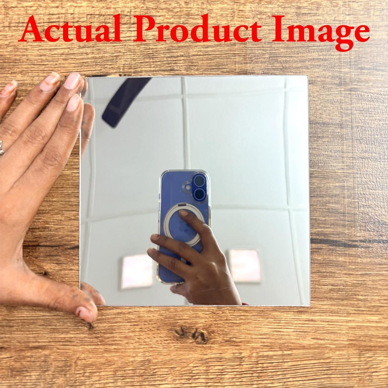 Square modern acrylic mirror stickers for living room held by hand on wooden surface reflecting phone and ceiling