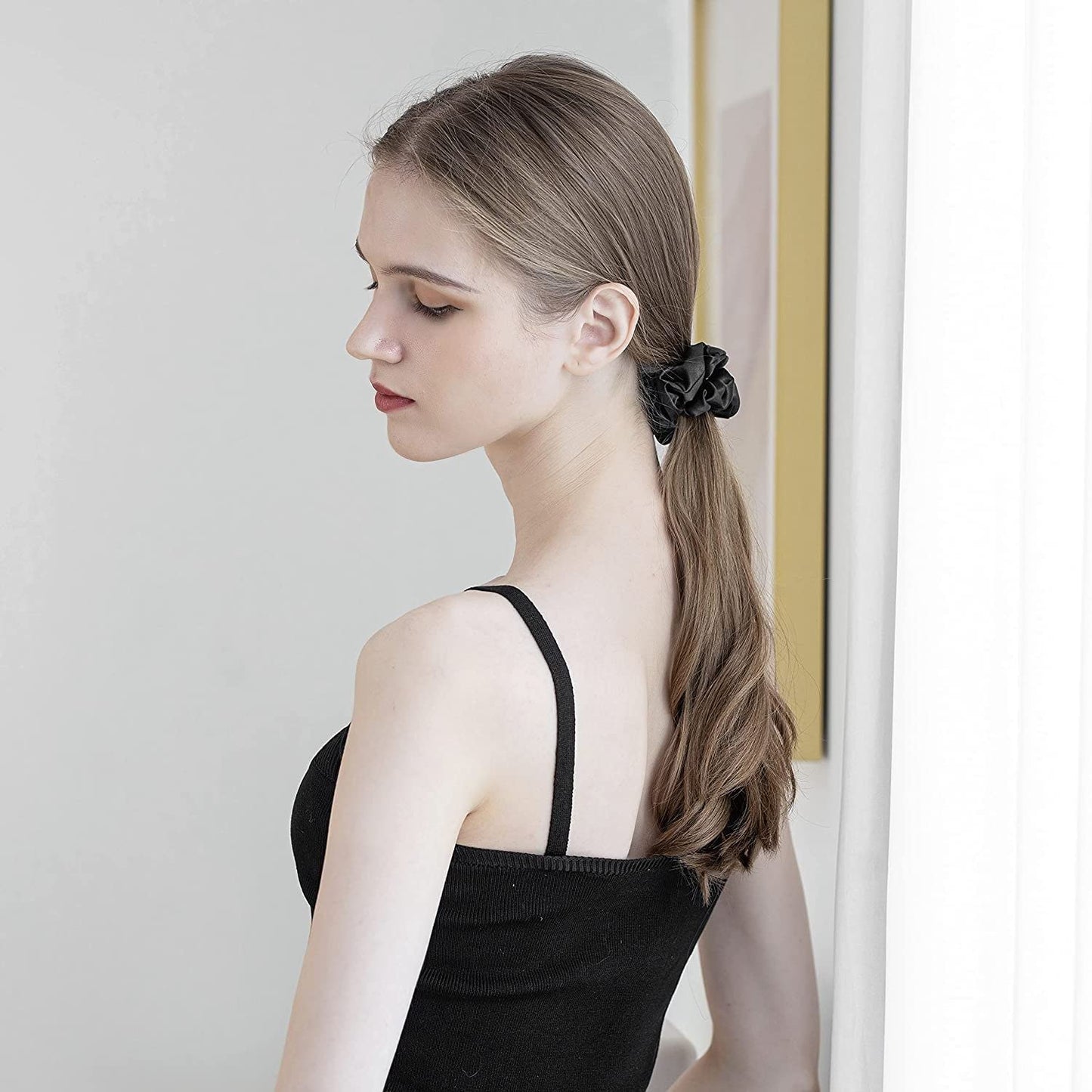 Woman with long brown hair wearing a black mulberry silk elastic band for hair holding a ponytail