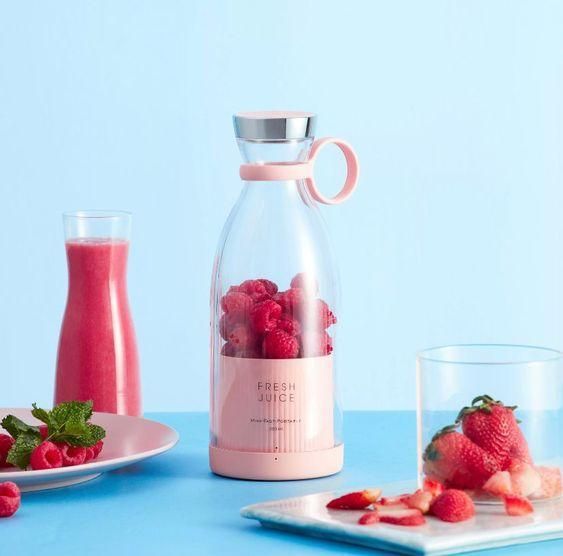 Pink compact blender for travel filled with raspberries surrounded by fresh fruit and smoothie on blue background