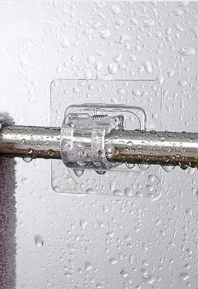 Clear multifunctional rod holder clips securely holding a metal rod on a wet glass surface