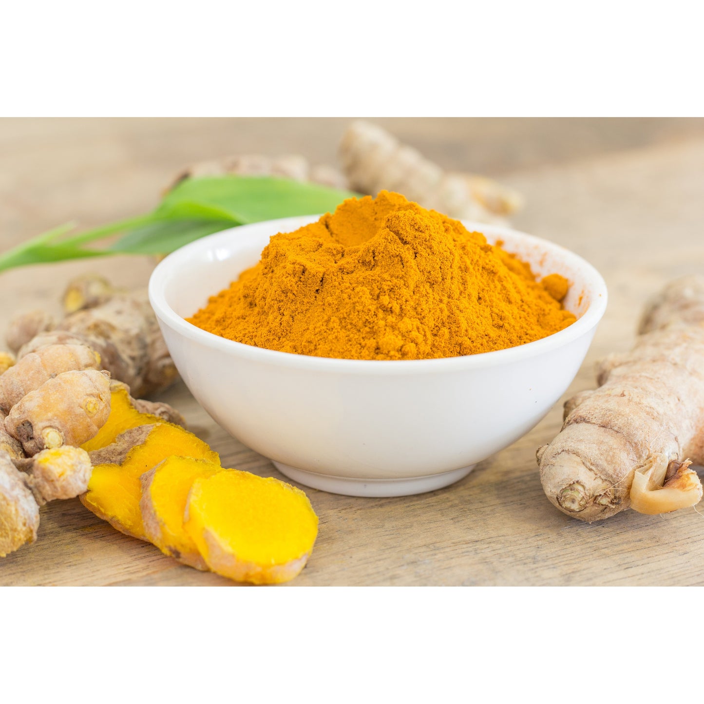 Organic haldi powder in a white bowl with fresh turmeric roots on a wooden surface