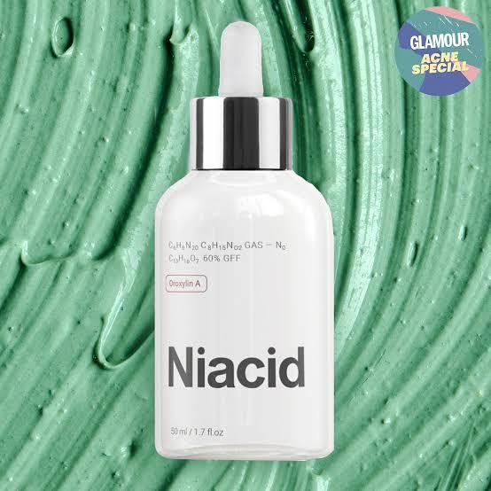 Organic niacid face serum in a glass dropper bottle against a green cream background