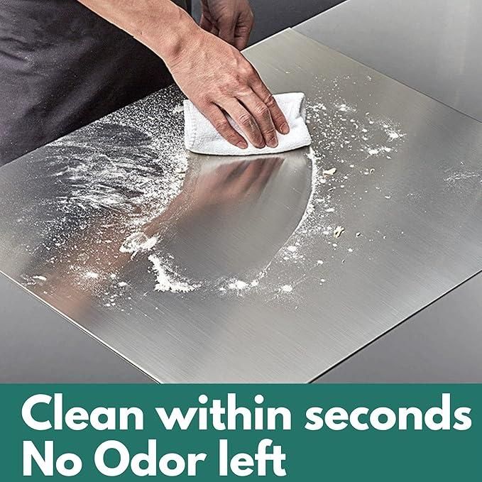 Person cleaning stainless steel chopping board with a white cloth on a kitchen counter
