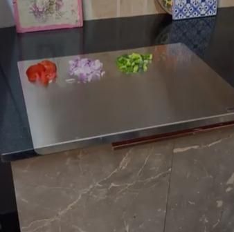 Stainless steel chopping board on kitchen countertop with chopped vegetables including tomatoes, onions, and green peppers