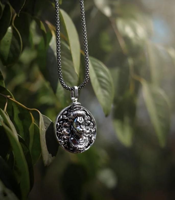 Religious silver Hanuman necklace pendant with detailed Hanuman design hanging on a chain against natural green leaves background