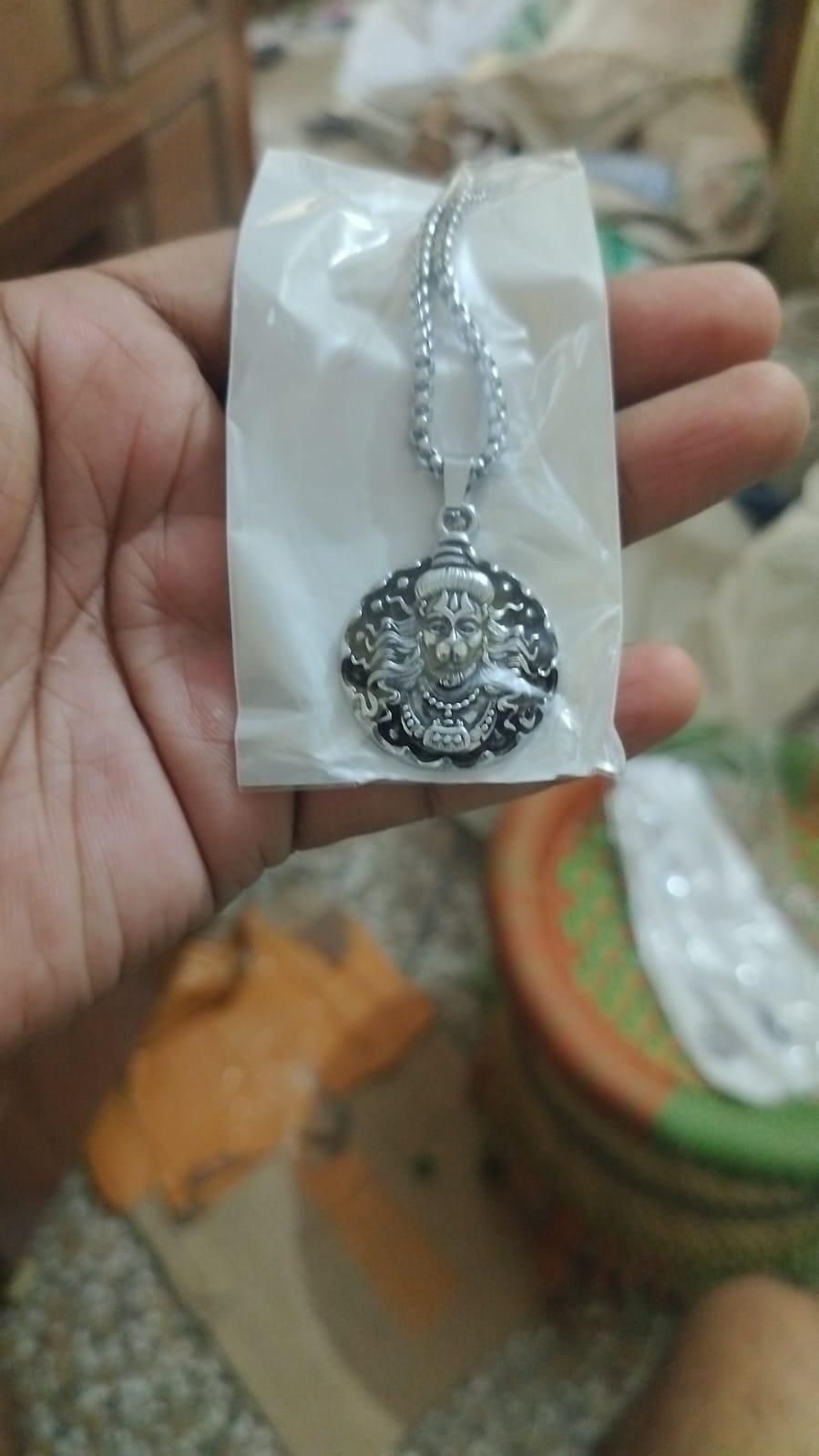 Religious silver Hanuman necklace with detailed pendant held in hand inside plastic packaging