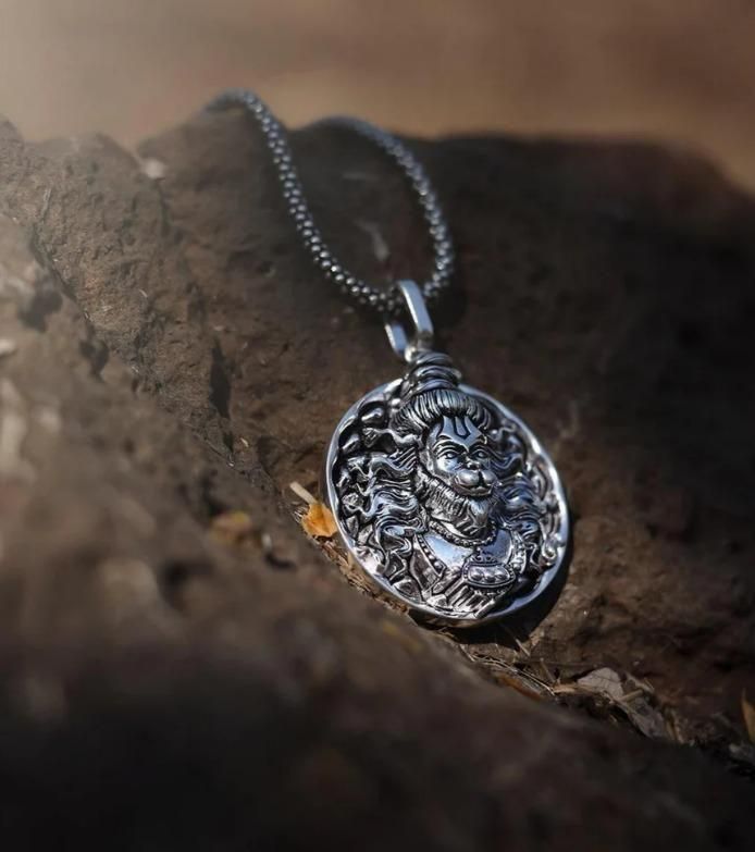 Religious silver Hanuman necklace with detailed pendant on a chain displayed on a natural rock surface