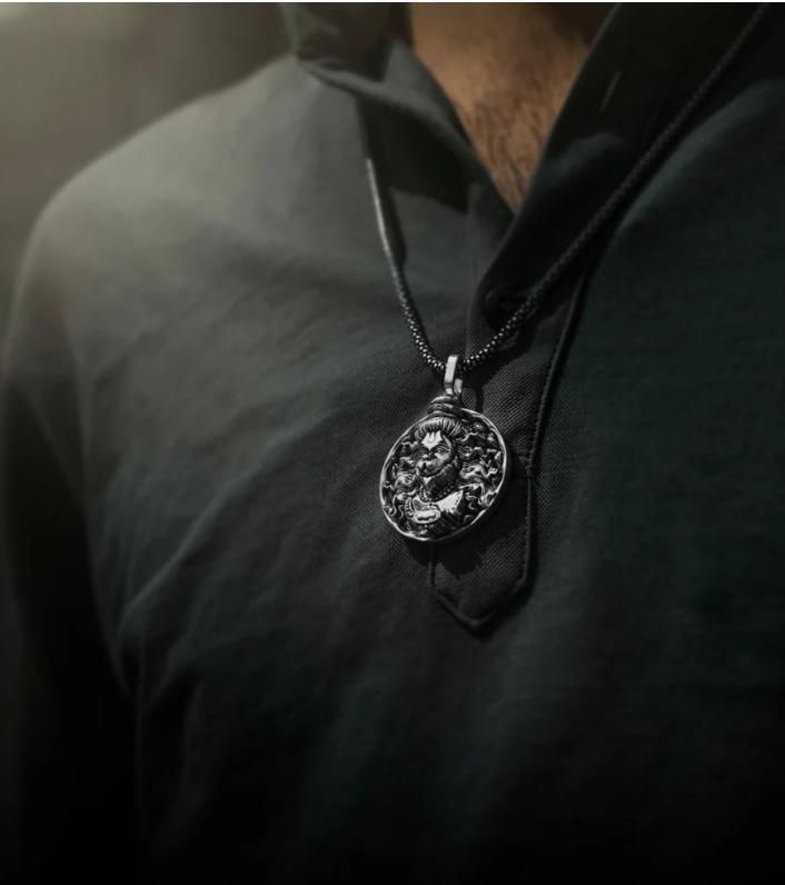 Close-up of a religious silver Hanuman necklace pendant worn on a black chain with a dark shirt background