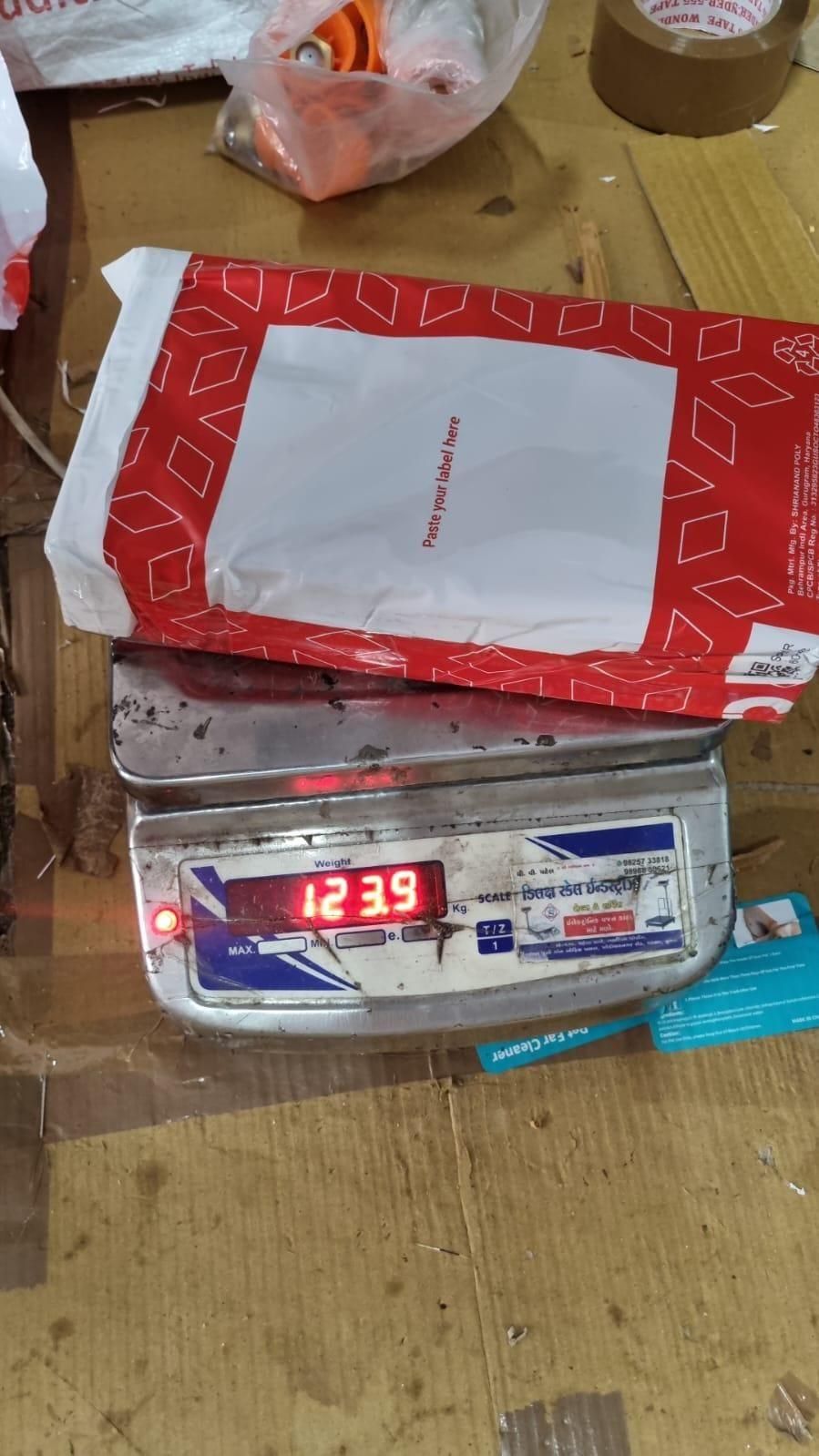 Red and white shipping package with pet hair removal gloves on digital scale reading about 124 grams on a cardboard workbench