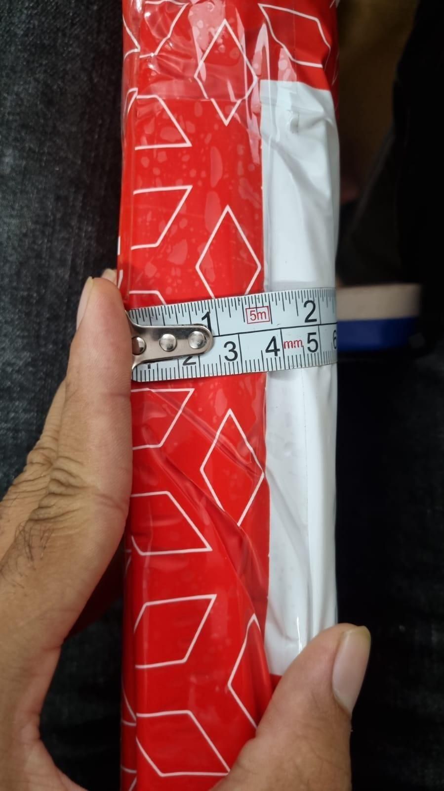 Hand measuring red and white packaged pet hair removal gloves roll with tape measure showing width