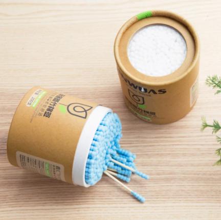 Soft wood stick cotton swabs with blue tips in eco-friendly round brown containers on wooden surface