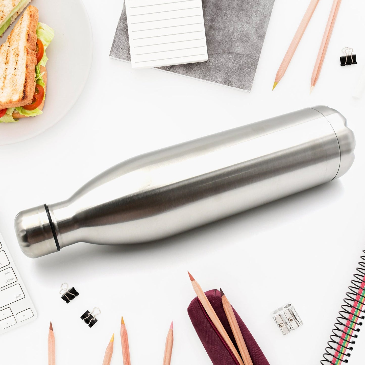 stainless steel double wall thermos bottle for travel on white desk with pencils and sandwich
