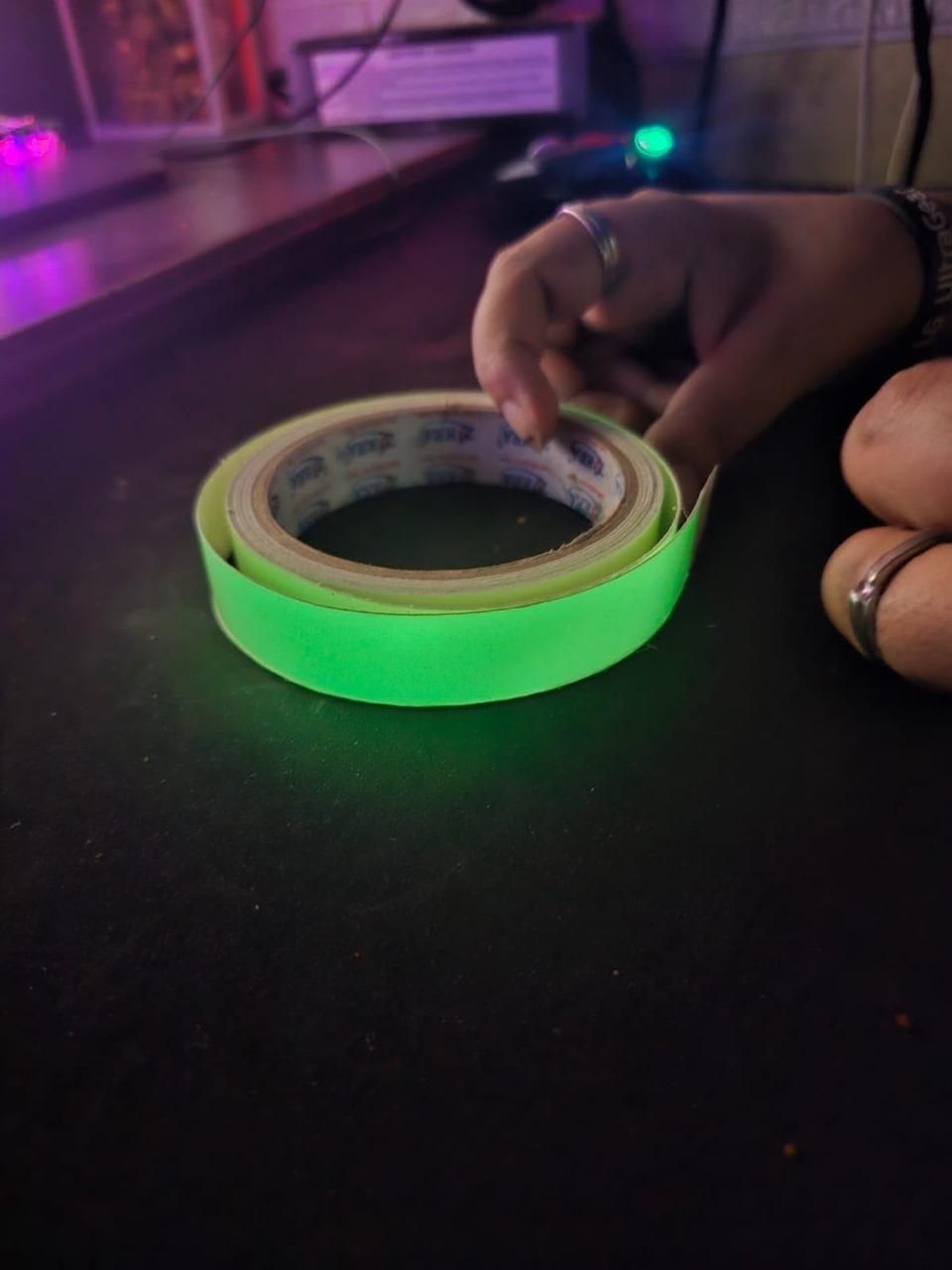 Roll of glow in the dark safety tape glowing bright green on a dark surface with a hand nearby