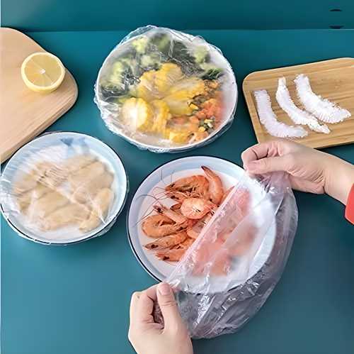 Reusable elastic plastic bags for food covering plates with shrimp, vegetables, and other dishes on a teal table