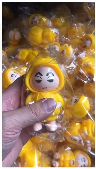Hand holding a Shinchan face changing keychain in yellow outfit among many similar keychains