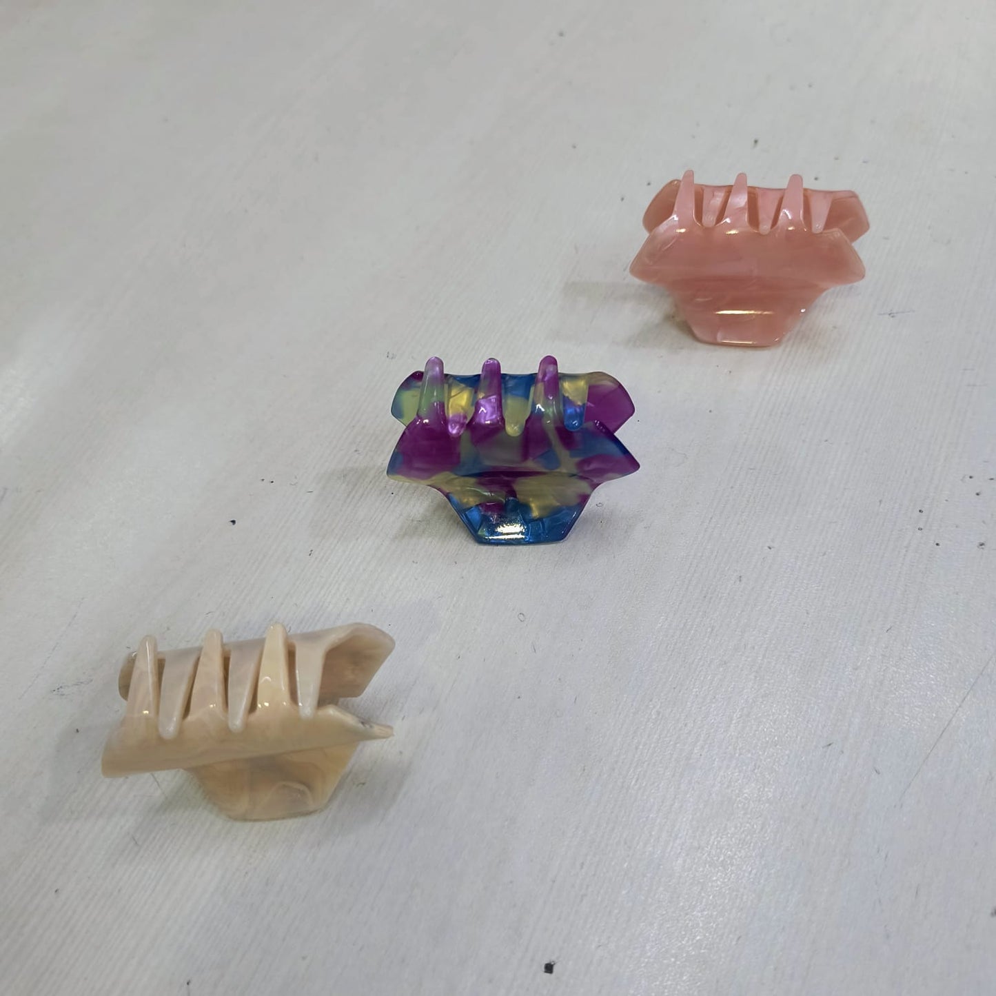Set of three small hair claw clips for women in pink, beige, and multicolor on white surface