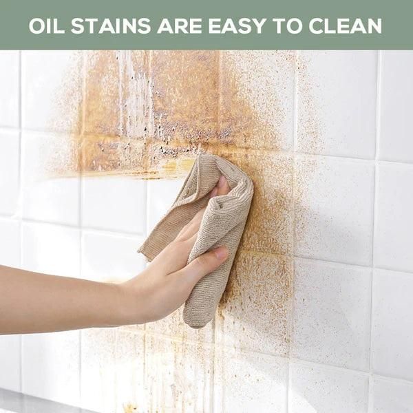 Hand cleaning oil stains on tiled wall with transparent wall protection film showing easy stain removal